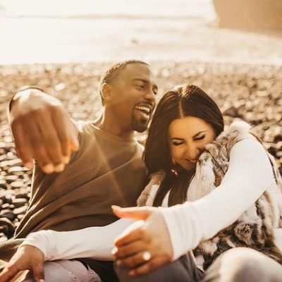 Both Jeffrey Jordan and Radina Aneva is sitting on the beach and laughing in the picture.